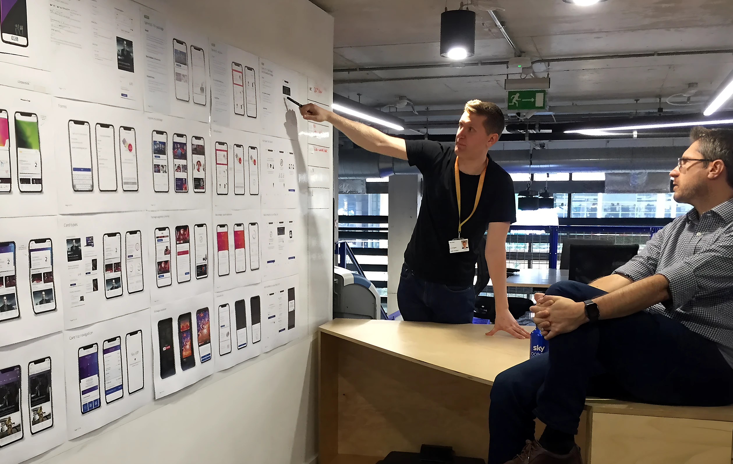 Phil pointing to designs on a wall while chatting with a colleague